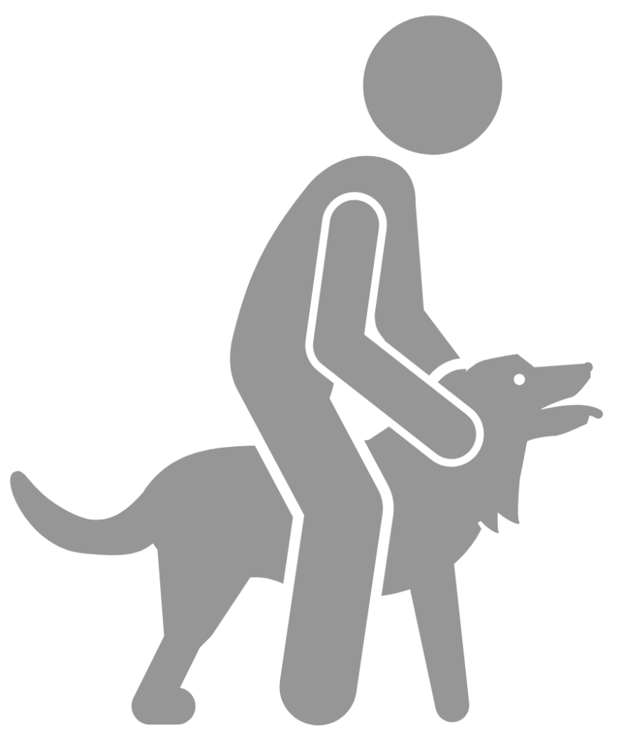 Das Bild zeigt eine stilisierte, graue Silhouette auf weißem Hintergrund. Eine stehende Person hält einen Hund sicher zwischen seinen Beinen startbereit mit beiden Händen fest. Der Hund blickt mit dem Kopf nach vorne und wirkt ruhig und entspannt. Das Halten symbolisiert die Startszene von Rettungshunden. Sie gibt dem Hund Fürsorge, Hilfestellung und Nähe.